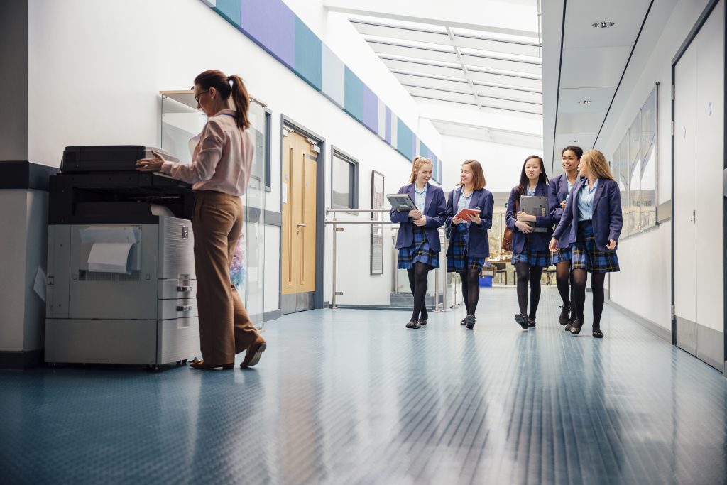 teacher using printer in school halls students walking