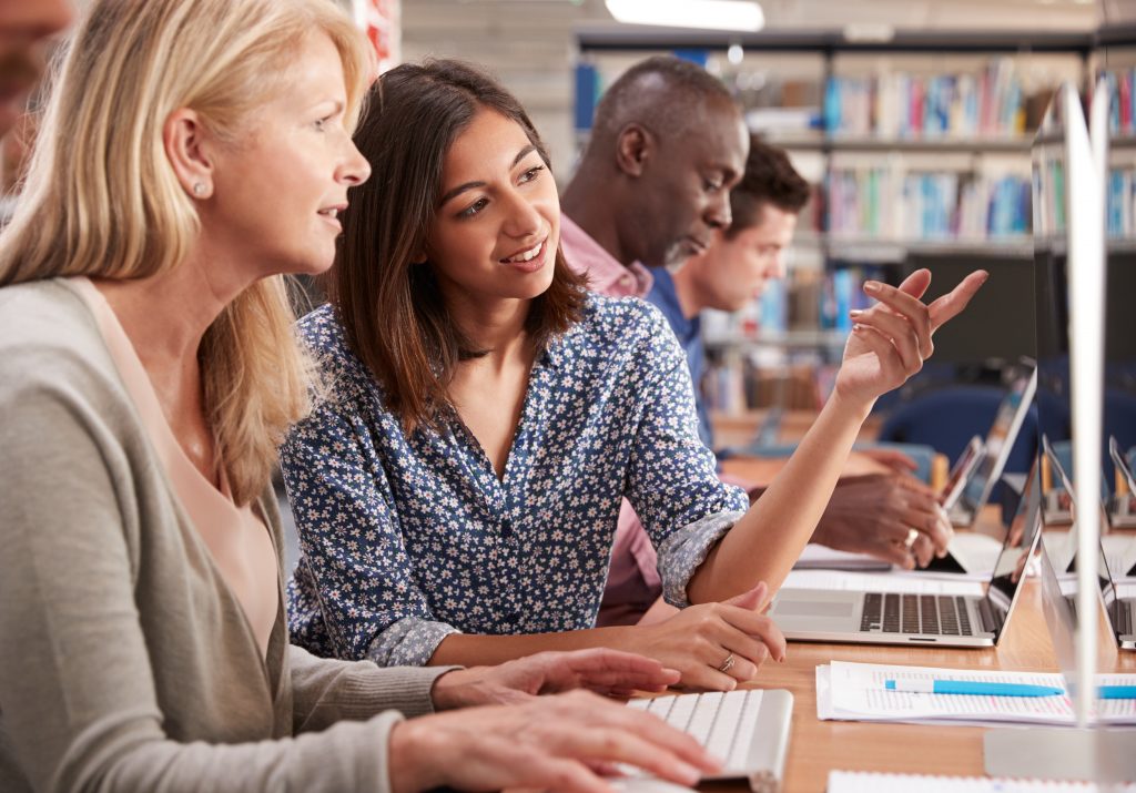 teacher helping mature student on computer