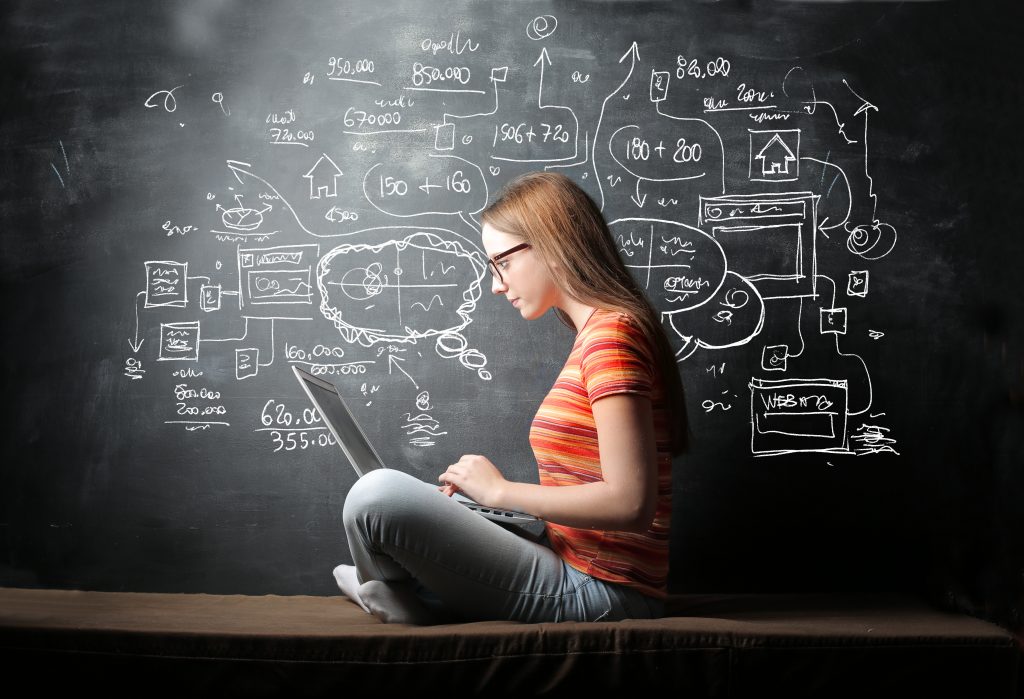 student sat on laptop by chalk board with technical drawings