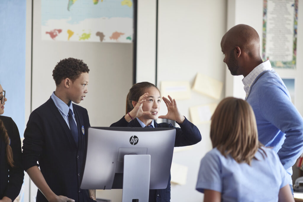 Students working together on a HP ProOne 400 AIO PC in class while a teacher supervises.