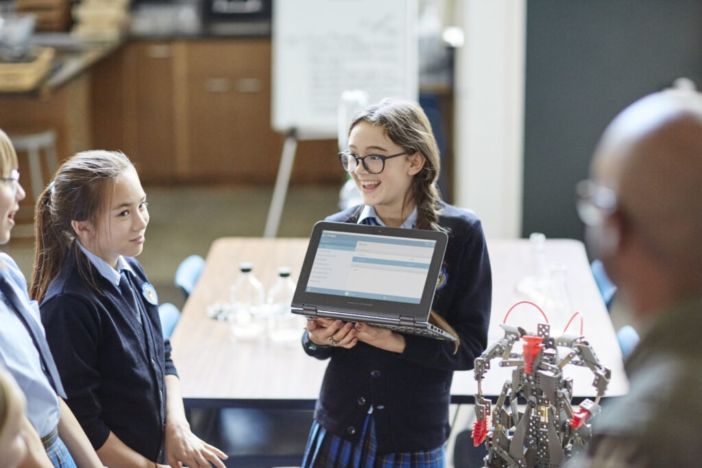 A child holding up a laptop for her classroom to see